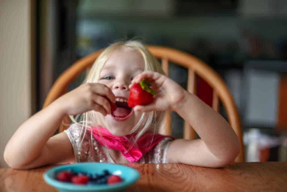 girl smiling and eating strawberries at the table