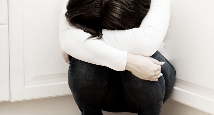 A woman crouched down in a corner with head buried in arms. 