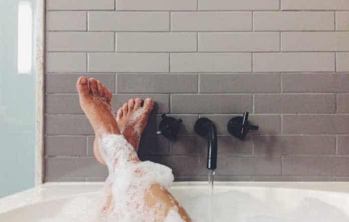 beautiful woman's feet sticking out of a soapy bathtub and relaxing on the tile surround after using essential oils for stress like tranquil. 