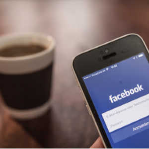 iphone with facebook open near cup of coffee