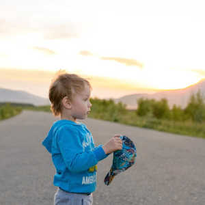 4 year old standing in country road watching sunset and holding baseball cap