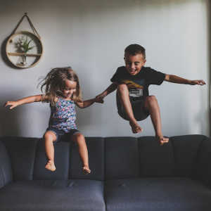 two strong willed kids jumping on the couch and laughing