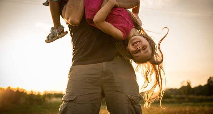 Dad holding strong willed daughter upside down while she laughs