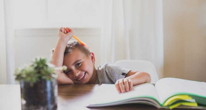Child focusing at table doing homework and smiling.