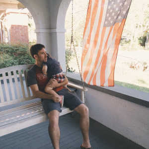 A man sitting on a bench holding his toddler son and hugging him.