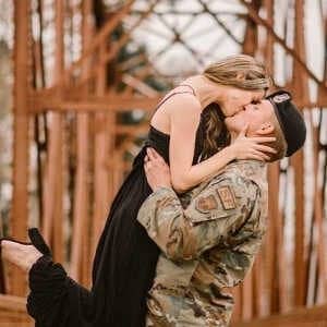 A woman kissing a military man in uniform on a bridge.