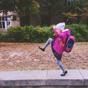 School-aged girl with backpack skipping down the sidewalk