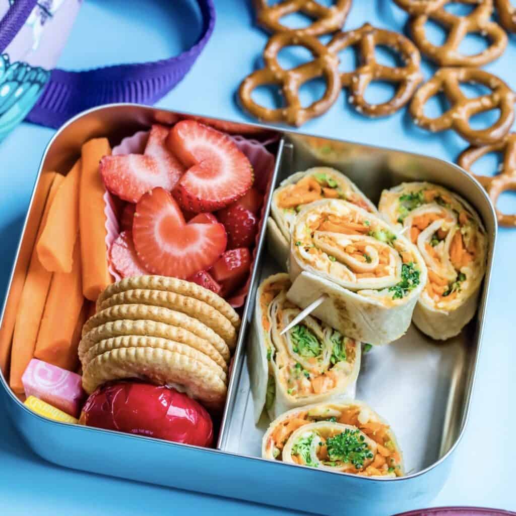 bento box with veggie hummus roll ups, strawberries, carrots and crackers