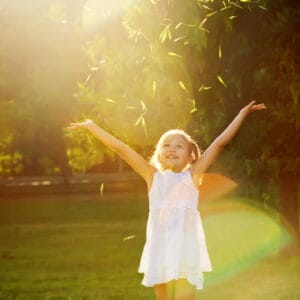 Child throwing leaves in the air and smiling with sun shining.