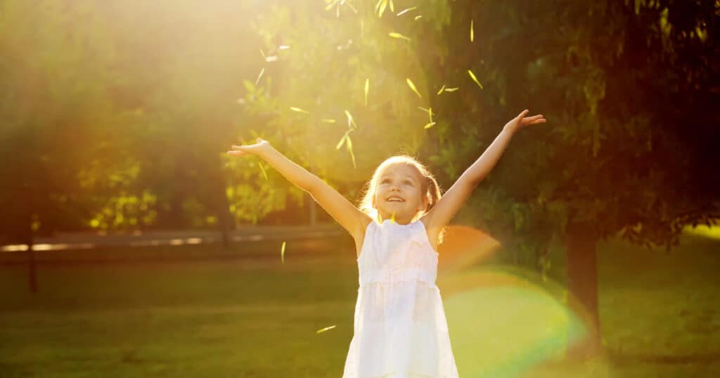 Child throwing leaves in the air and smiling with sun shining. 