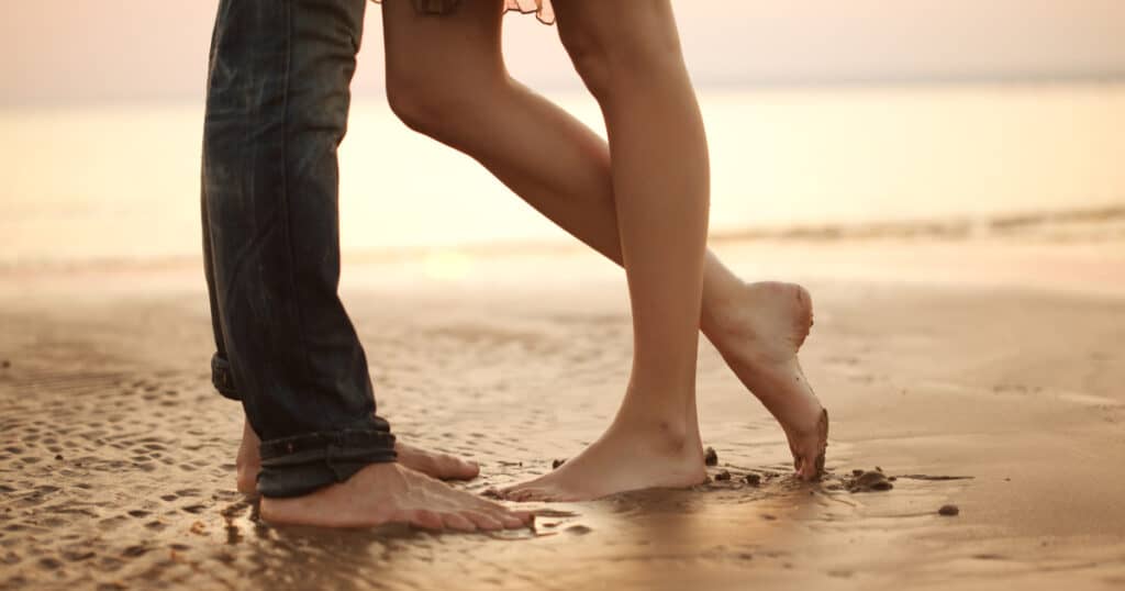 sepasang kaki berdiri berdekatan satu sama lain tanpa alas kaki di pantai