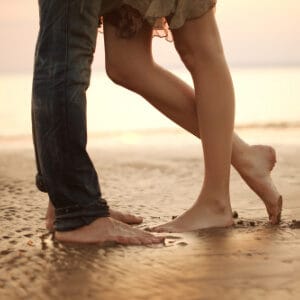 A loving young couple hugging and kissing on the beach. Two lovers man and woman barefoot in the wet sand.